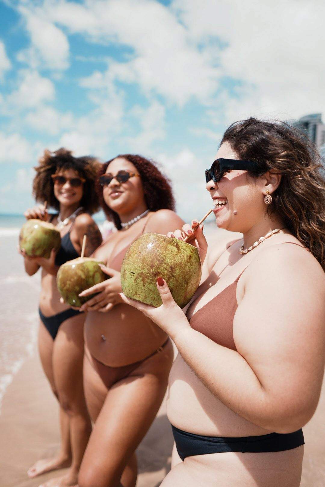 Letícia, Giselle e Larissa de biquíni na beira do mar, tomando água de coco