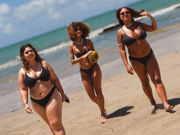 Três mulheres de biquíni caminhando na beira do mar