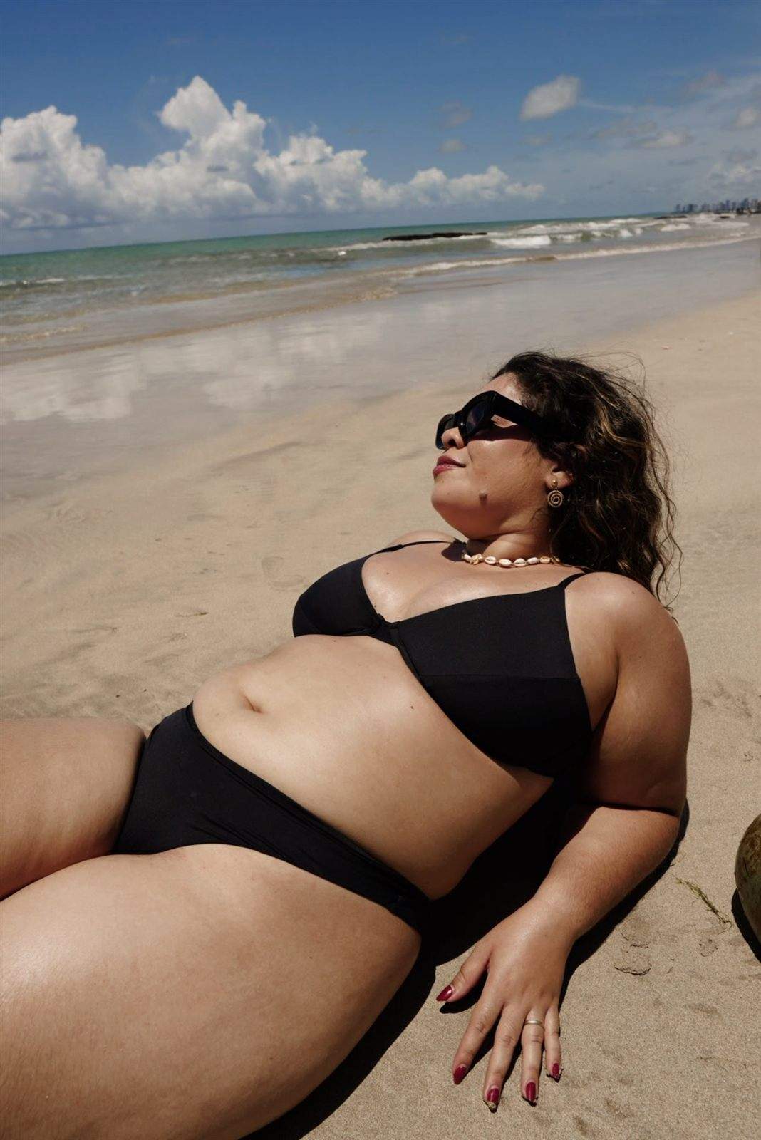 Mulher de biquíni preto deitada na areia, tomando sol